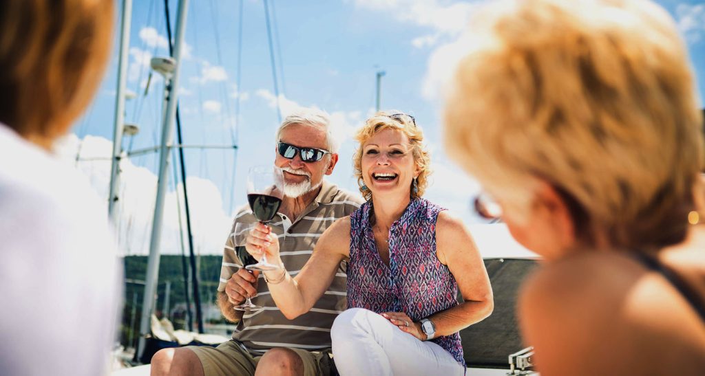 Active adults sitting on a boat near our 55+ community in Minnetonka. They are holding glasses of wine and smiling.