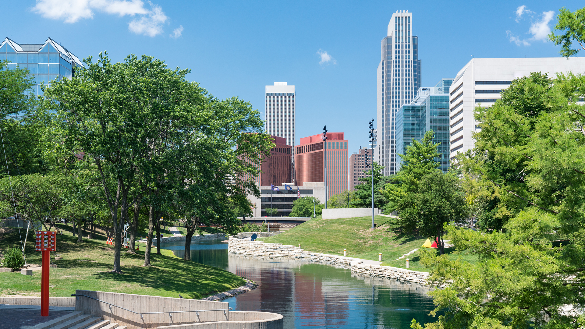 The riverfront in the city of Omaha with a view grassy hills, trees, the water, and the city skyline.