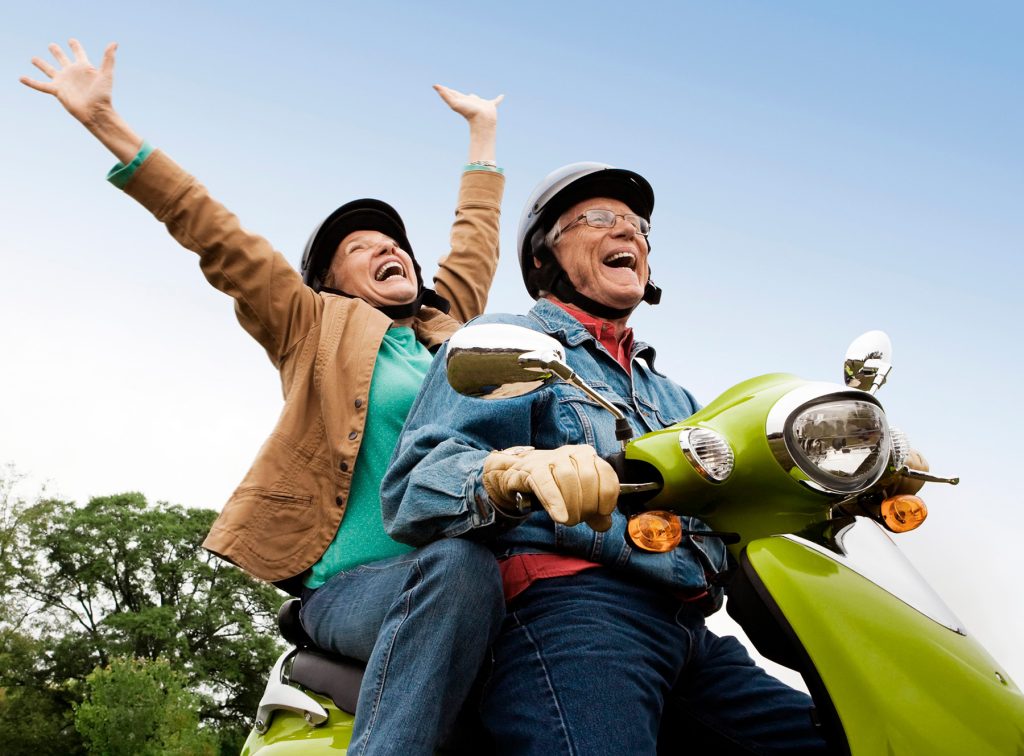 Two people riding a vespa, as seen from below. They are smiling and throwing their hands in the air.